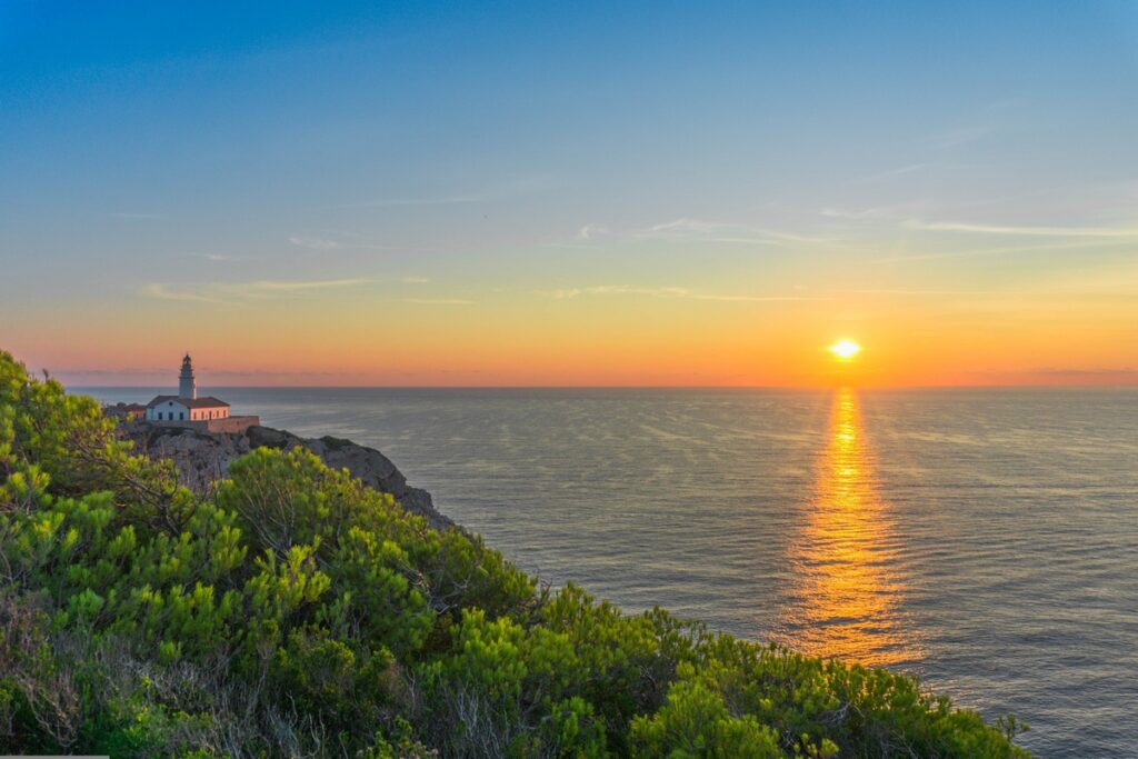Leuchtturm auf grüner Insel vor Sonnenuntergang über dem Meer